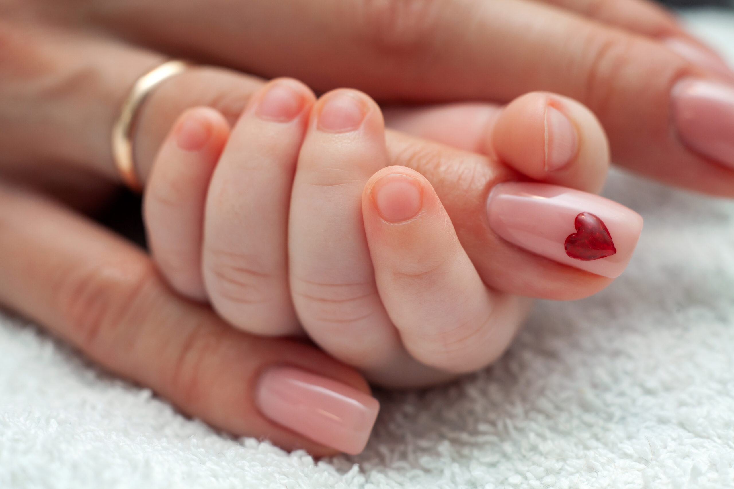 Infant holding mommy's finger. Mum taking care of the infant baby. Heart sign on mom's nail. Family, motherhood, love concept.