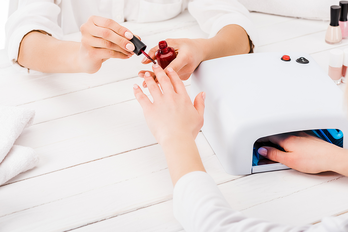 Partial view of woman dries nail polish while manicurist painting fingers in red